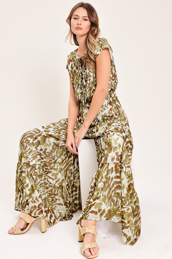 Woman wearing an olive green, brown, and white patterned woven jumpsuit featuring round neckline, short sleeve, front tie detail, elastic waist and tier wide leg pant | Flying Tomato