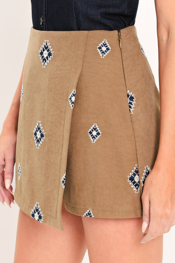 A woman wearing a camel wrap-style mini skort with a navy and white geometric diamond pattern | Flying Tomato