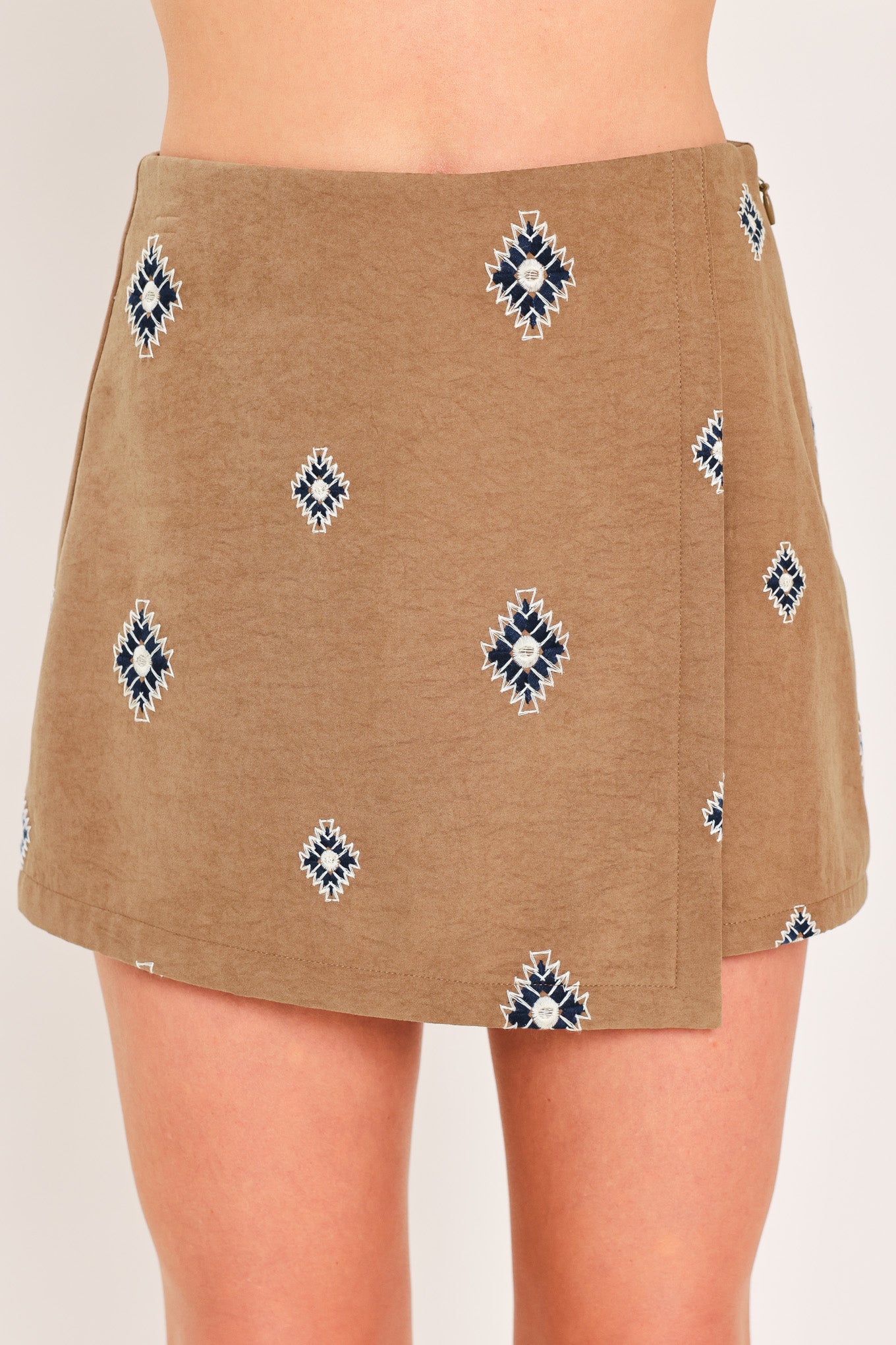 A woman wearing a camel wrap-style mini skort with a navy and white geometric diamond pattern | Flying Tomato