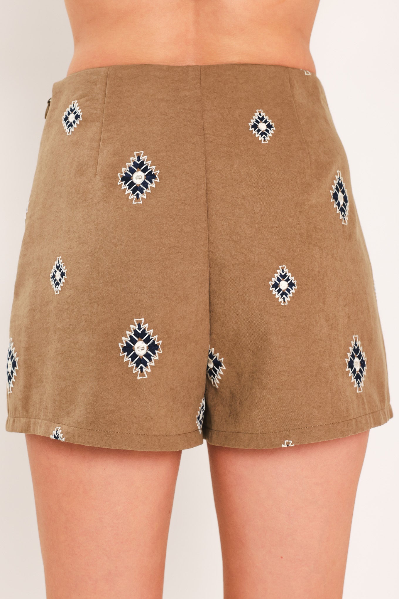 A woman wearing a camel wrap-style mini skort with a navy and white geometric diamond pattern | Flying Tomato