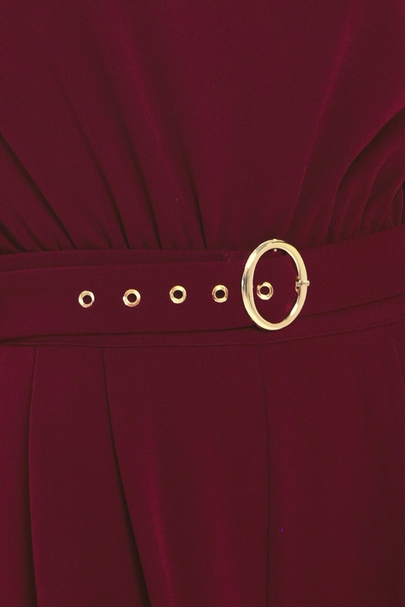 A woman modeling a sleeveless, high-neck, wide-leg jumpsuit in deep burgundy. The jumpsuit features a matching belt with a gold-tone buckle at the waist | Flying Tomato