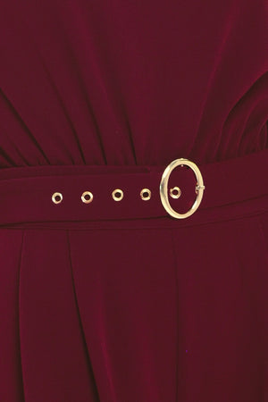 A woman modeling a sleeveless, high-neck, wide-leg jumpsuit in deep burgundy. The jumpsuit features a matching belt with a gold-tone buckle at the waist | Flying Tomato