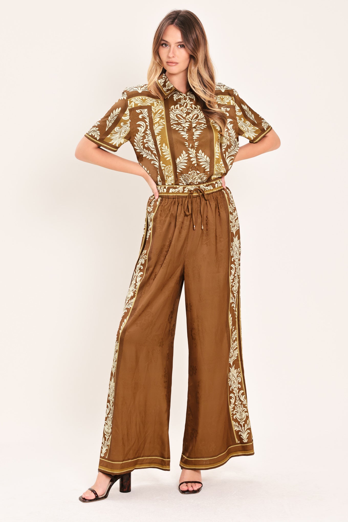 Woman wearing camel brown wide-leg pants with white floral embroidery on the side and waistband | Flying Tomato
