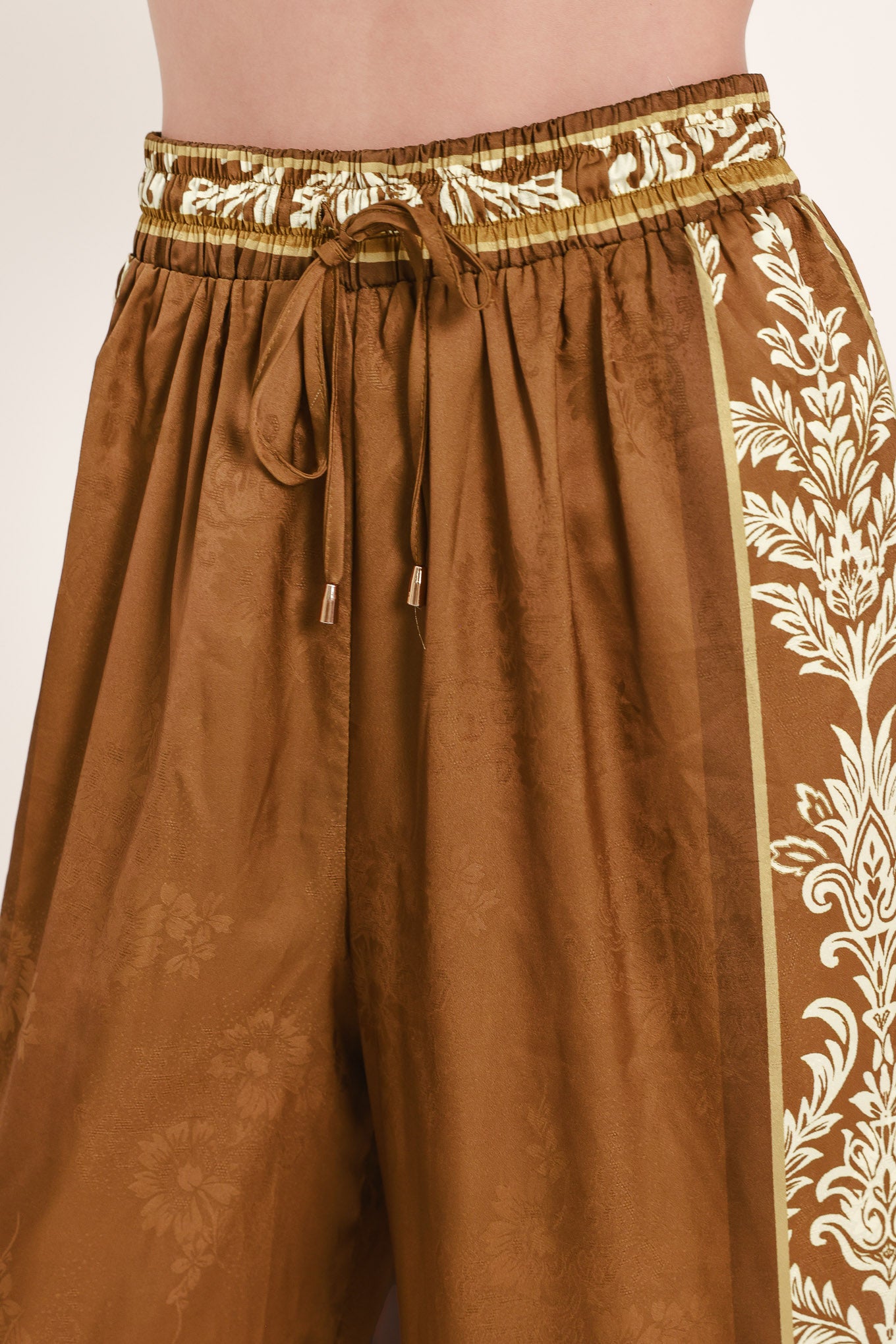 Woman wearing camel brown wide-leg pants with white floral embroidery on the side and waistband | Flying Tomato