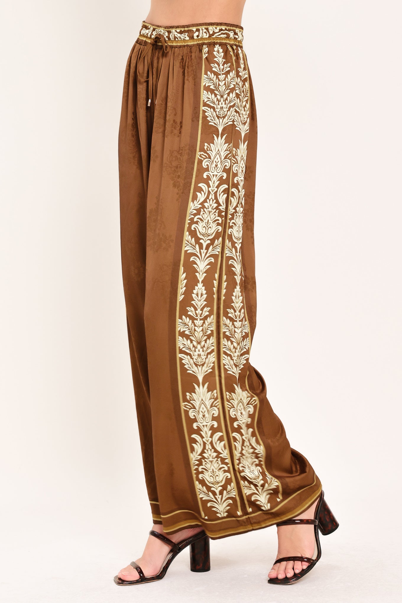 Woman wearing camel brown wide-leg pants with white floral embroidery on the side and waistband | Flying Tomato