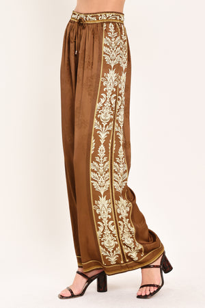 Woman wearing camel brown wide-leg pants with white floral embroidery on the side and waistband | Flying Tomato