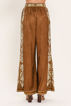 Woman wearing camel brown wide-leg pants with white floral embroidery on the side and waistband | Flying Tomato