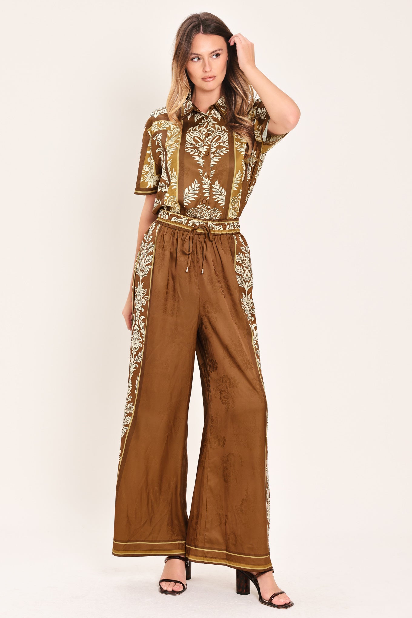 Woman wearing camel brown wide-leg pants with white floral embroidery on the side and waistband | Flying Tomato