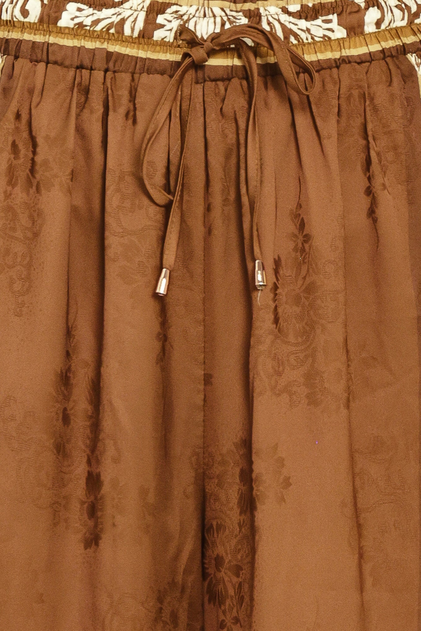 Woman wearing camel brown wide-leg pants with white floral embroidery on the side and waistband | Flying Tomato