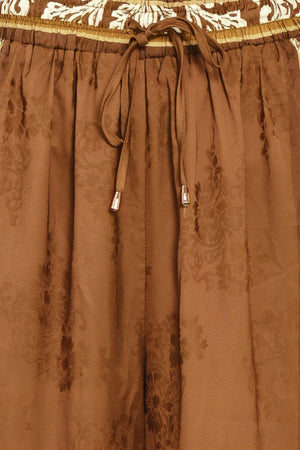 Woman wearing camel brown wide-leg pants with white floral embroidery on the side and waistband | Flying Tomato