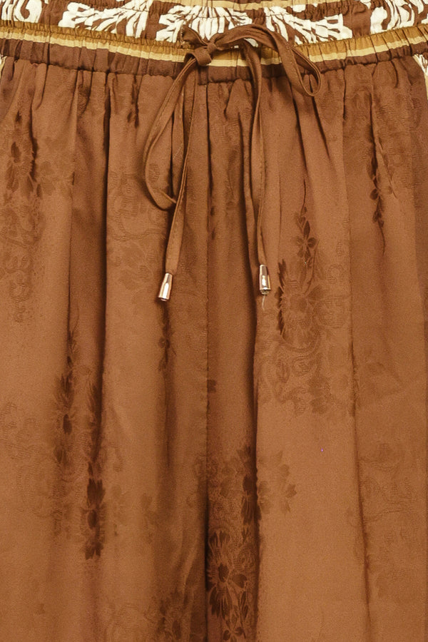 Woman wearing camel brown wide-leg pants with white floral embroidery on the side and waistband | Flying Tomato