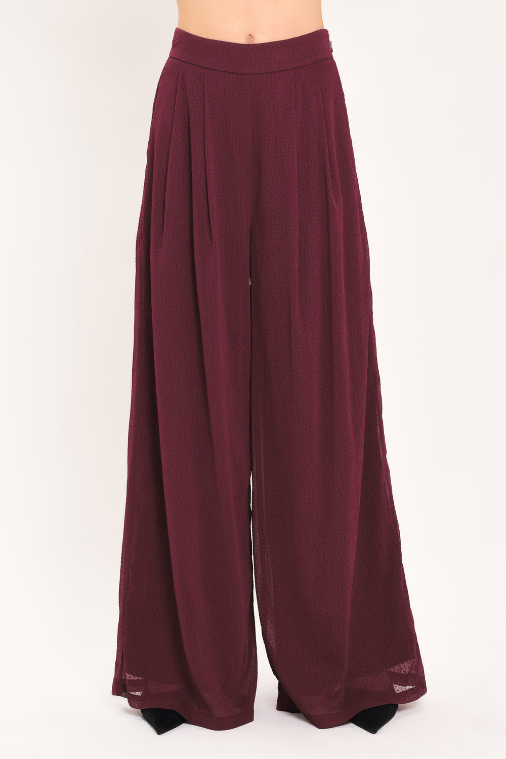 A pair of wide-leg, high-waisted trousers in a deep burgundy or maroon fabric, shown on a model | Flying Tomato