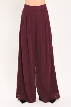 A pair of wide-leg, high-waisted trousers in a deep burgundy or maroon fabric, shown on a model | Flying Tomato