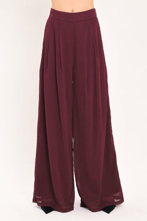 A pair of wide-leg, high-waisted trousers in a deep burgundy or maroon fabric, shown on a model | Flying Tomato