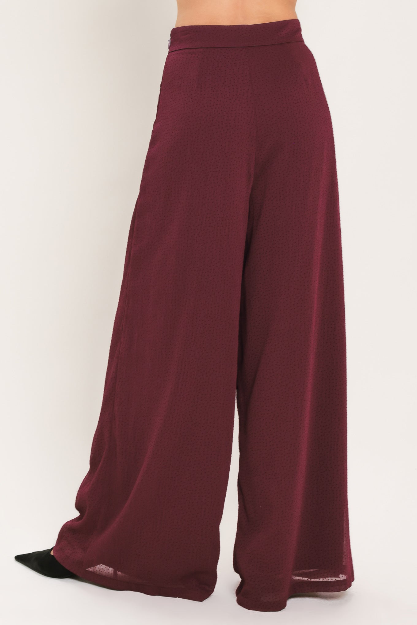 A pair of wide-leg, high-waisted trousers in a deep burgundy or maroon fabric, shown on a model | Flying Tomato