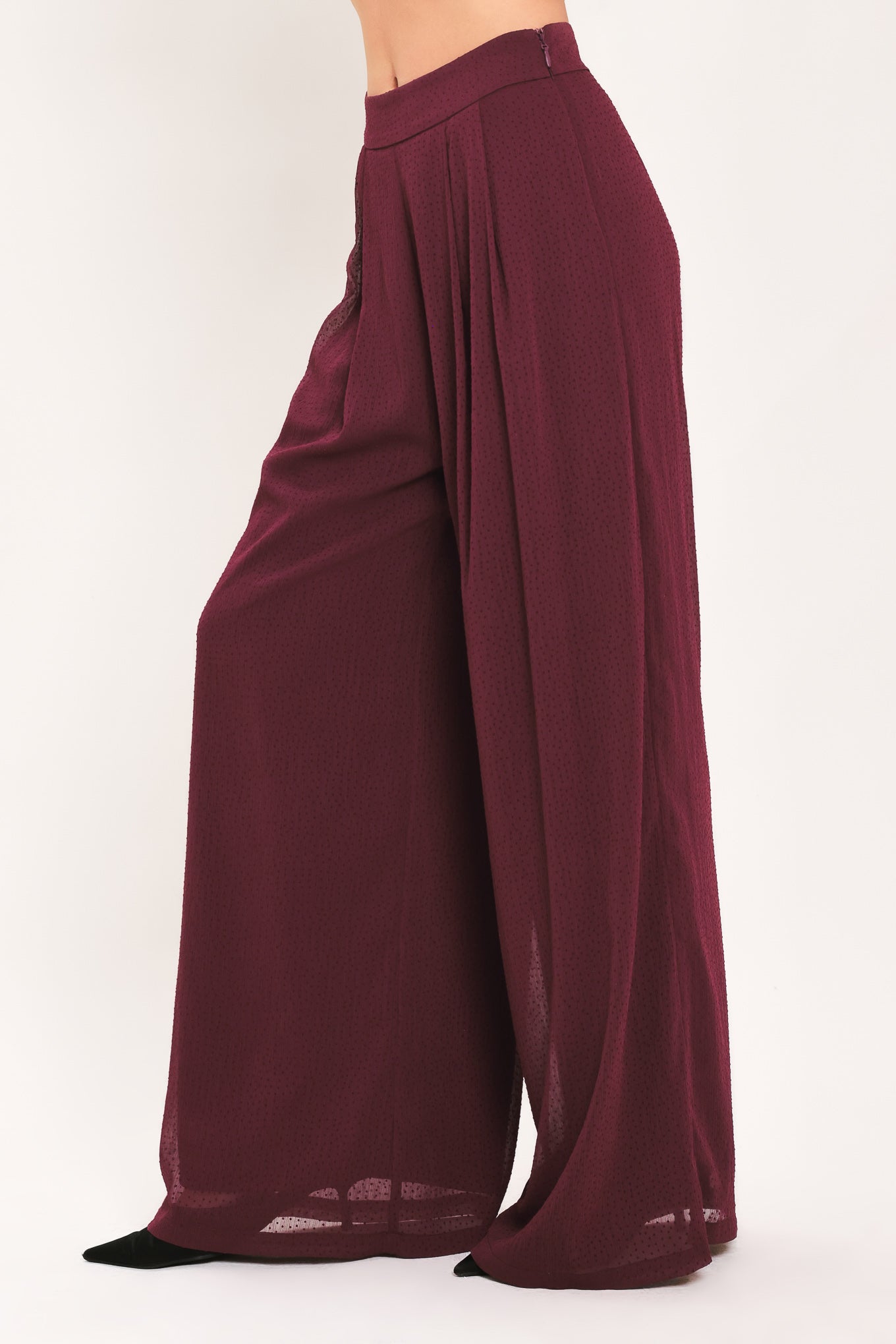 A pair of wide-leg, high-waisted trousers in a deep burgundy or maroon fabric, shown on a model | Flying Tomato