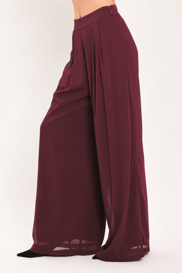 A pair of wide-leg, high-waisted trousers in a deep burgundy or maroon fabric, shown on a model | Flying Tomato