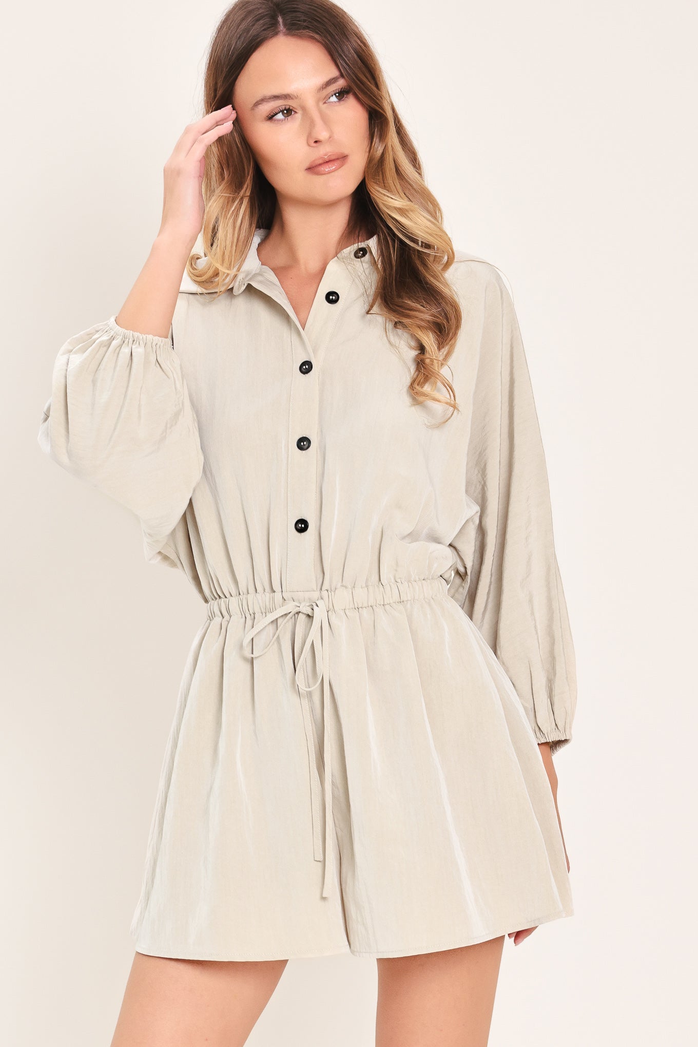 Woman wearing a light gray, stone colored romper featuring collar, front button down, 3/4 dolman sleeve and elastic waist with tie | Flying Tomato
