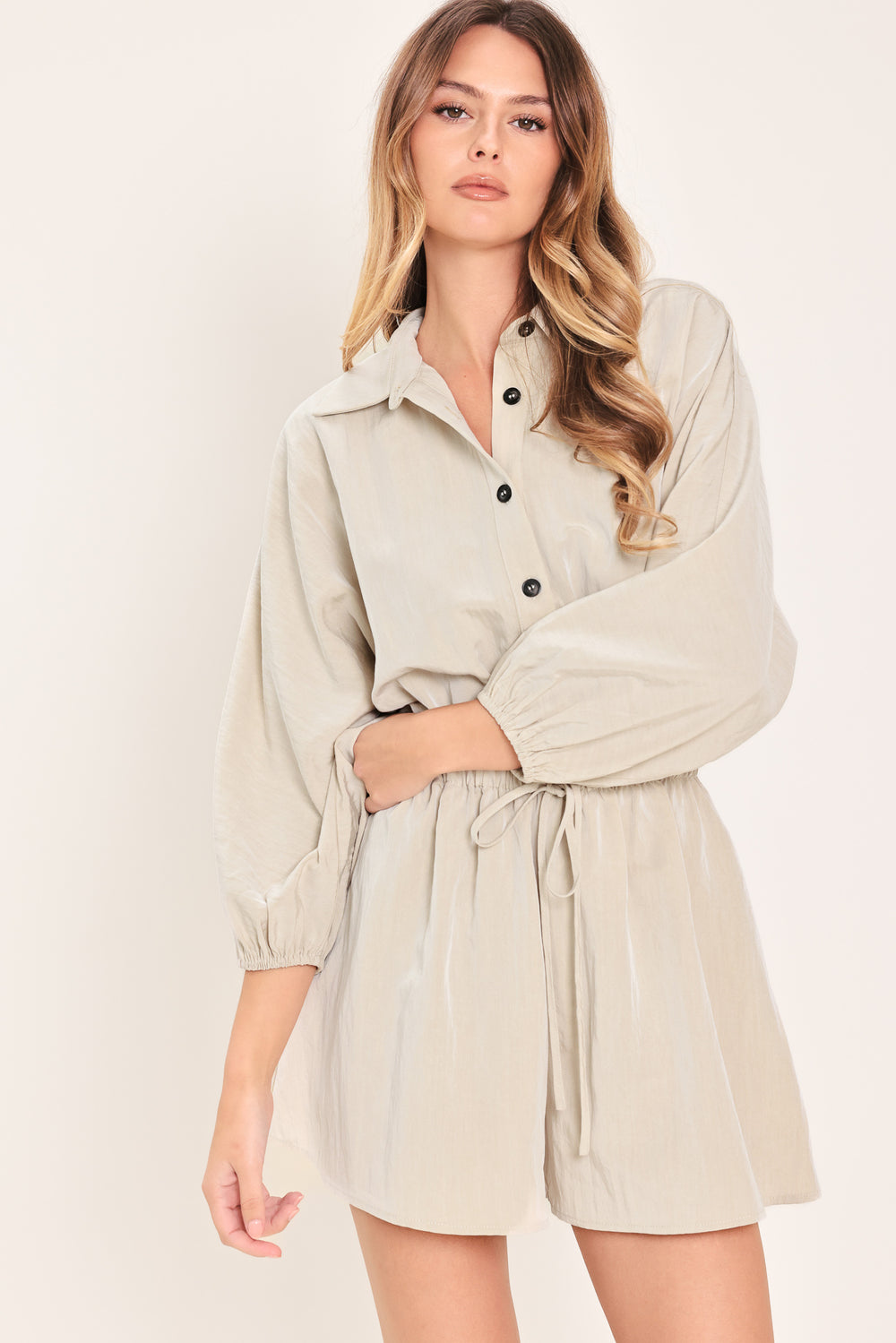 Woman wearing a light gray, stone colored romper featuring collar, front button down, 3/4 dolman sleeve and elastic waist with tie | Flying Tomato