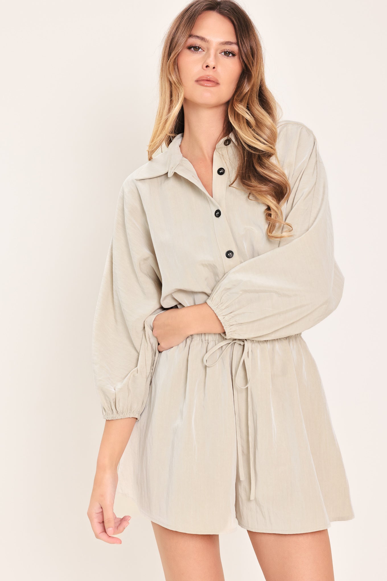 Woman wearing a light gray, stone colored romper featuring collar, front button down, 3/4 dolman sleeve and elastic waist with tie | Flying Tomato