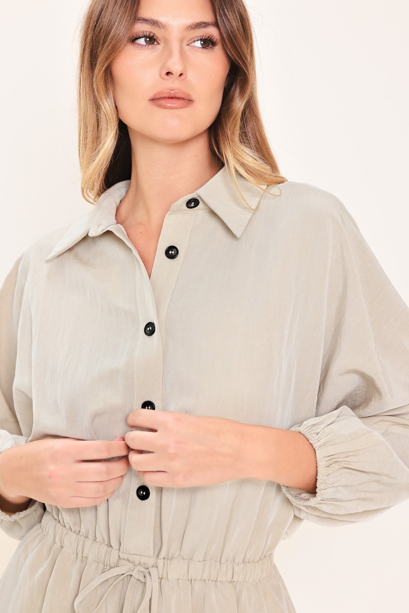 Woman wearing a light gray, stone colored romper featuring collar, front button down, 3/4 dolman sleeve and elastic waist with tie | Flying Tomato
