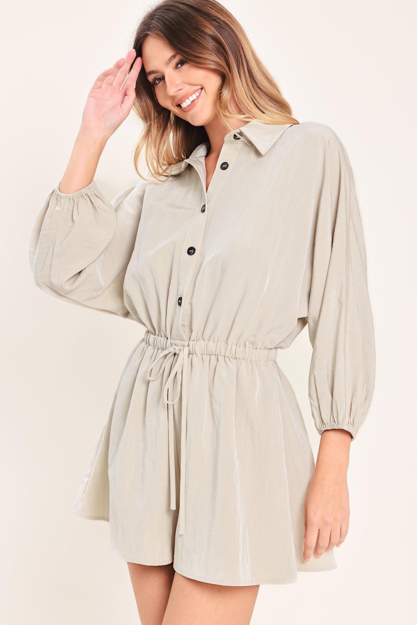 Woman wearing a light gray, stone colored romper featuring collar, front button down, 3/4 dolman sleeve and elastic waist with tie | Flying Tomato