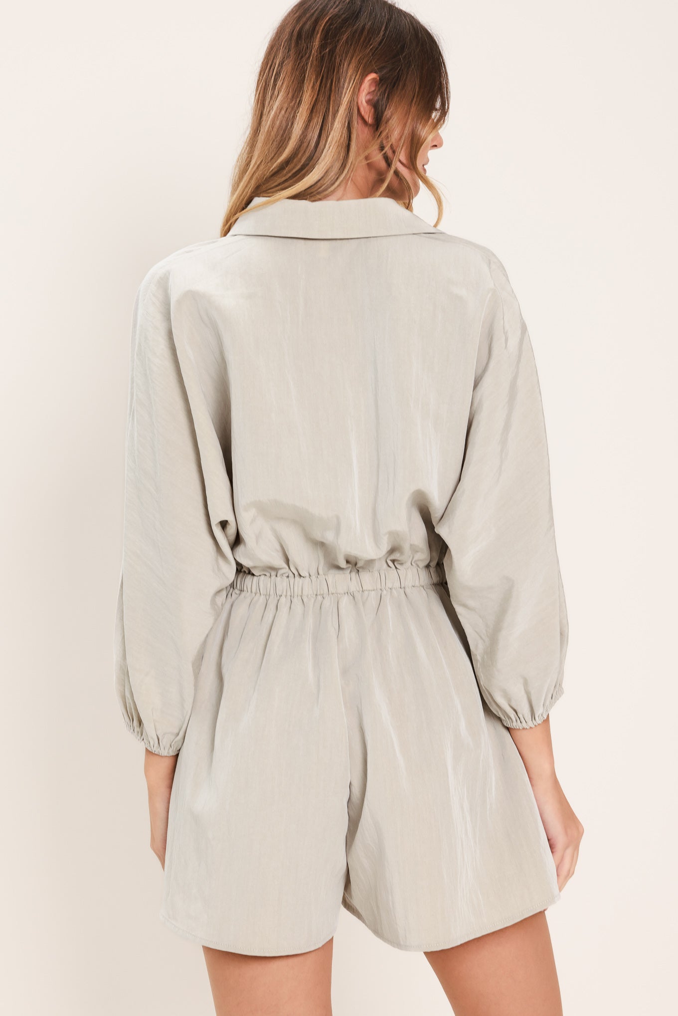 Woman wearing a light gray, stone colored romper featuring collar, front button down, 3/4 dolman sleeve and elastic waist with tie | Flying Tomato