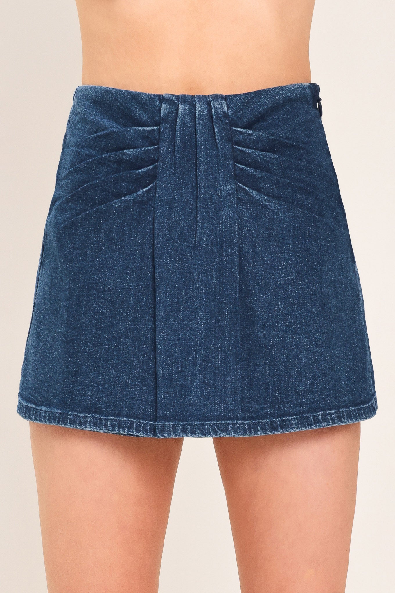 A close-up of a model wearing a dark blue denim mini skort with pleated detailing at the waistband | Flying Tomato