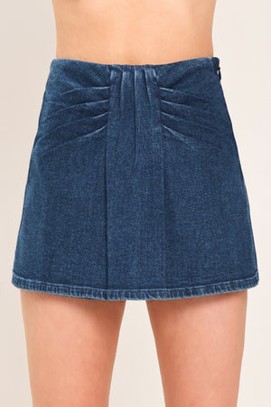 A close-up of a model wearing a dark blue denim mini skort with pleated detailing at the waistband | Flying Tomato