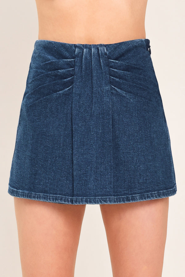 A close-up of a model wearing a dark blue denim mini skort with pleated detailing at the waistband | Flying Tomato