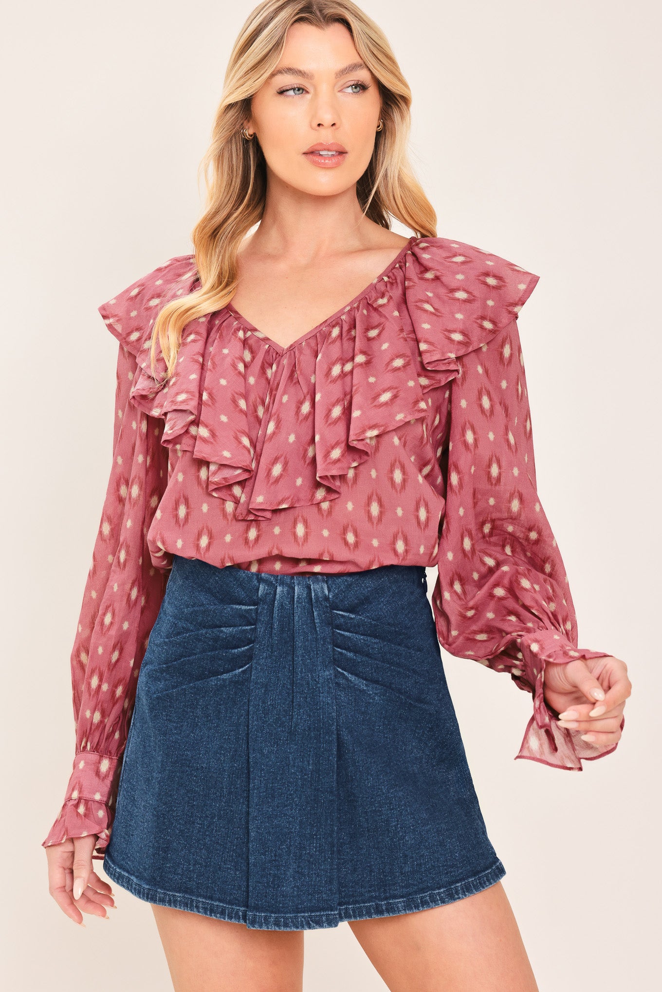 A woman wearing a dusty rose long-sleeve blouse with a white geometric pattern and layered ruffles, paired with a dark blue denim mini skort | Flying Tomato