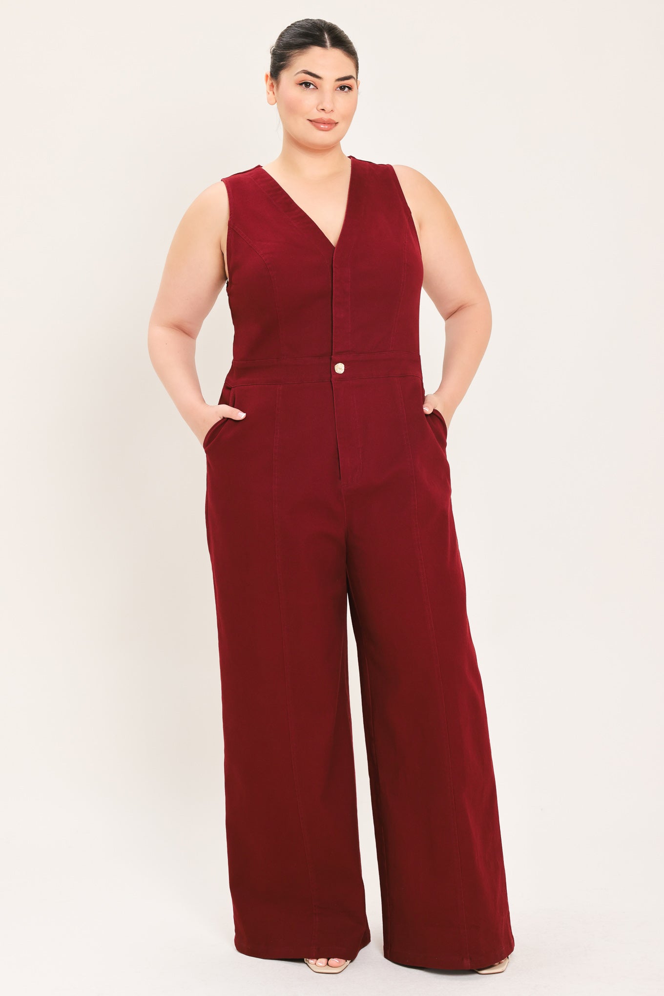 A woman modeling a sleeveless burgundy wide-leg jumpsuit with a V-neckline and front button detail | Plus Curve Flying Tomato