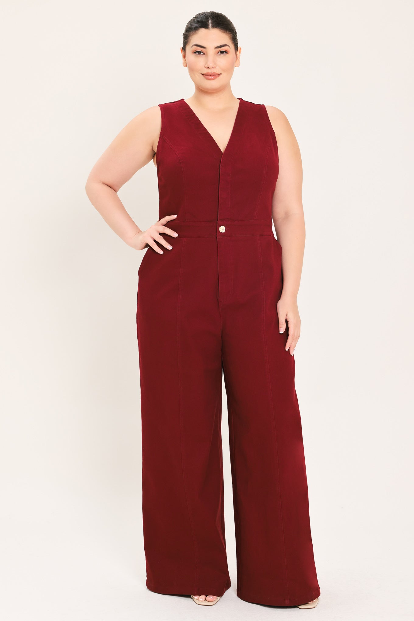 A woman modeling a sleeveless burgundy wide-leg jumpsuit with a V-neckline and front button detail | Plus Curve Flying Tomato