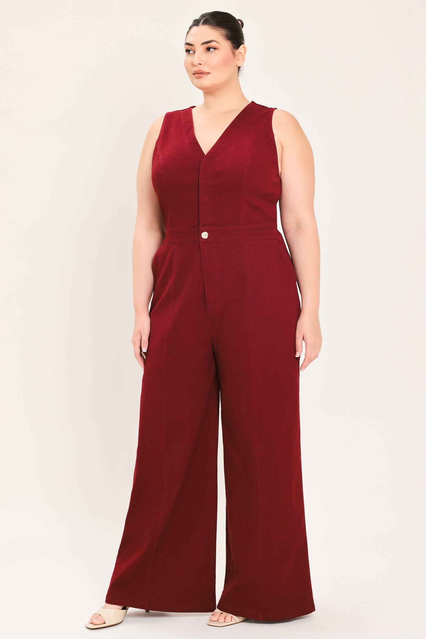 A woman modeling a sleeveless burgundy wide-leg jumpsuit with a V-neckline and front button detail | Plus Curve Flying Tomato