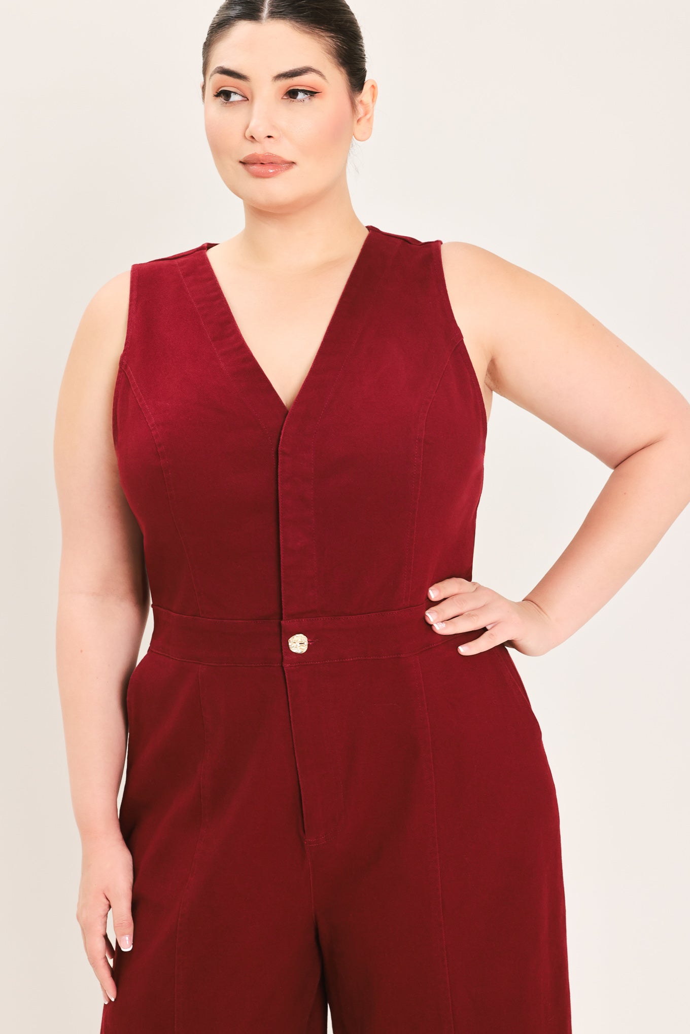 A woman modeling a sleeveless burgundy wide-leg jumpsuit with a V-neckline and front button detail | Plus Curve Flying Tomato