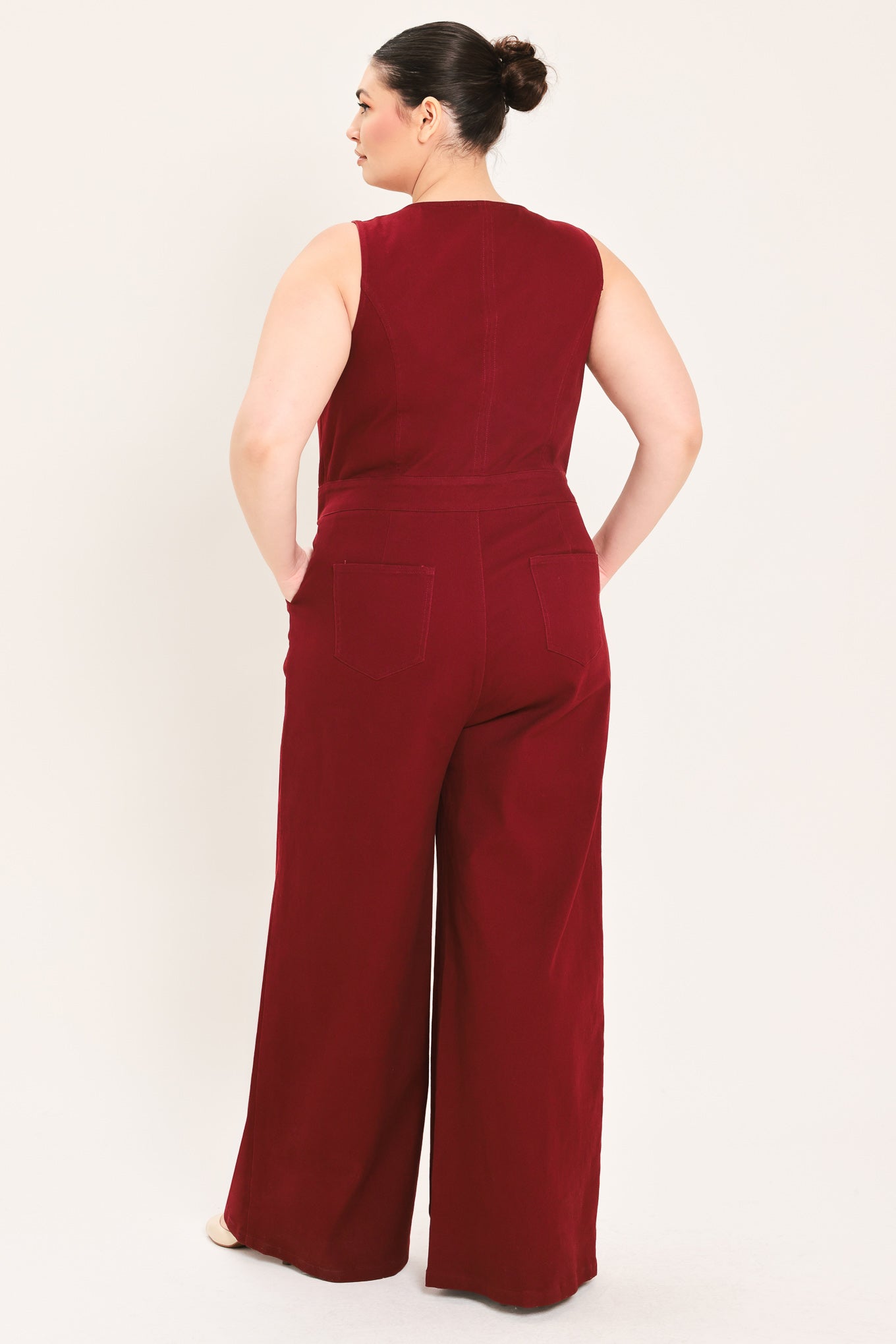 A woman modeling a sleeveless burgundy wide-leg jumpsuit with a V-neckline and front button detail | Plus Curve Flying Tomato