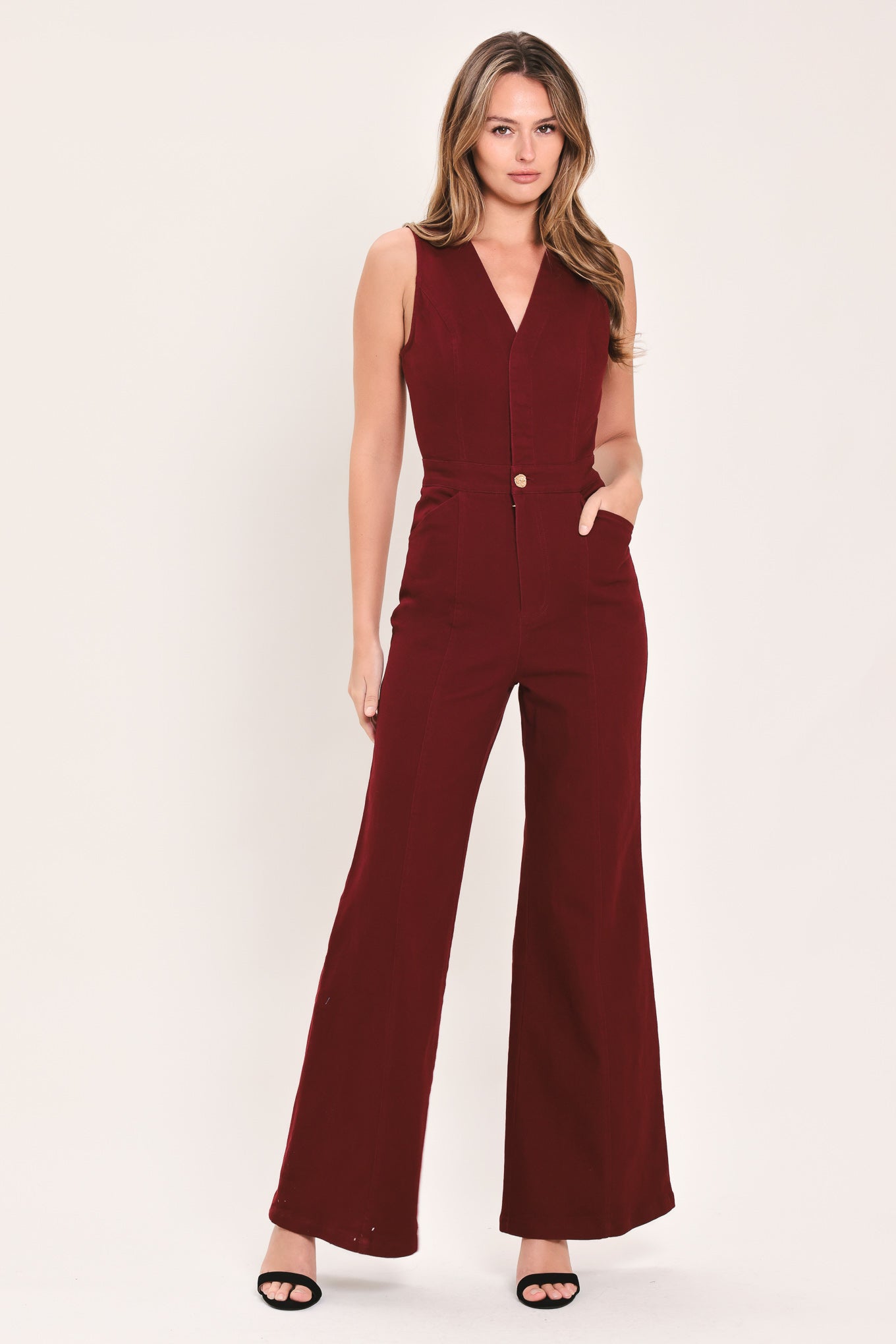 A woman wearing a sleeveless, deep burgundy jumpsuit with a V-neckline, front buttons, and wide-leg pants | Flying Tomato