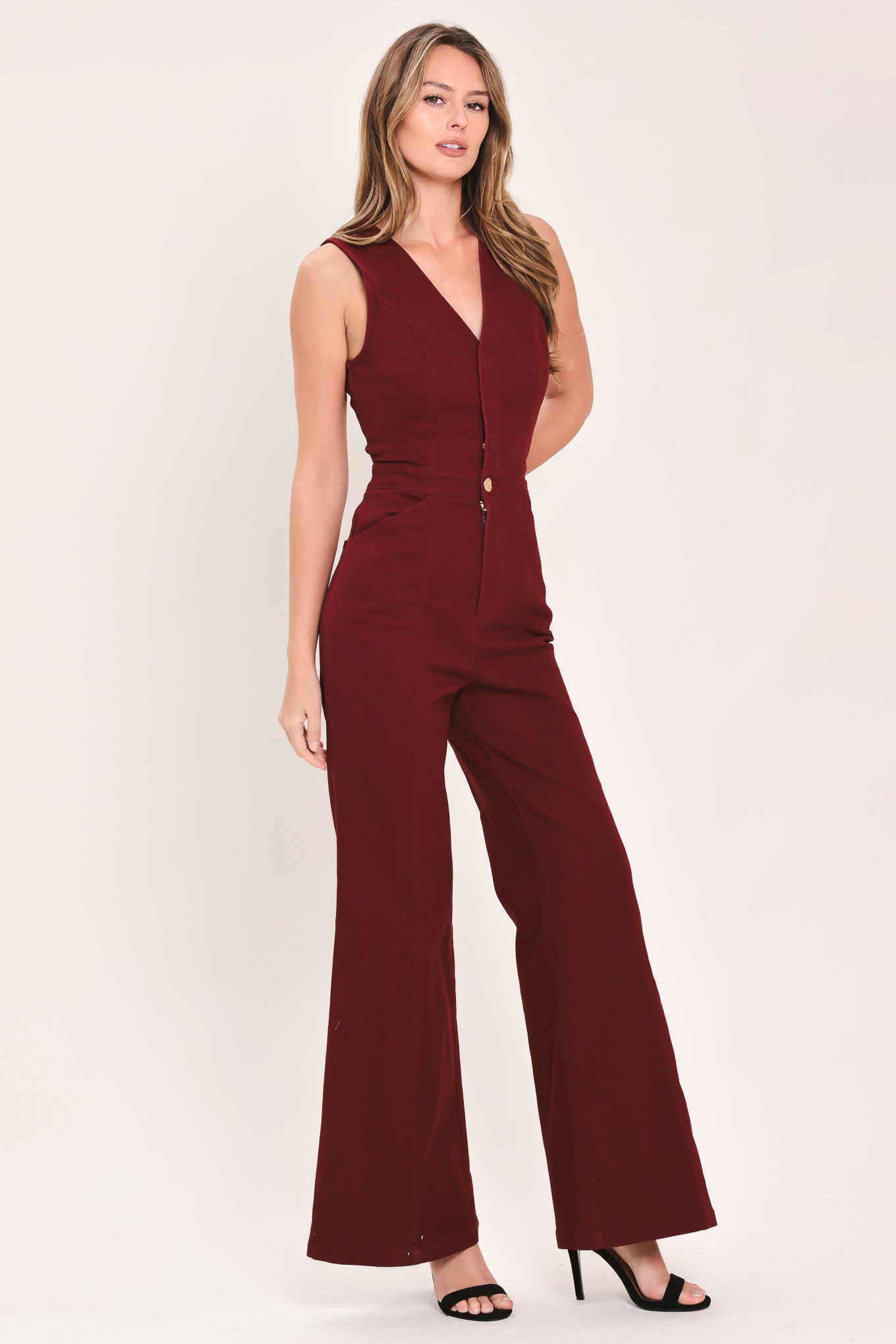 A woman wearing a sleeveless, deep burgundy jumpsuit with a V-neckline, front buttons, and wide-leg pants | Flying Tomato