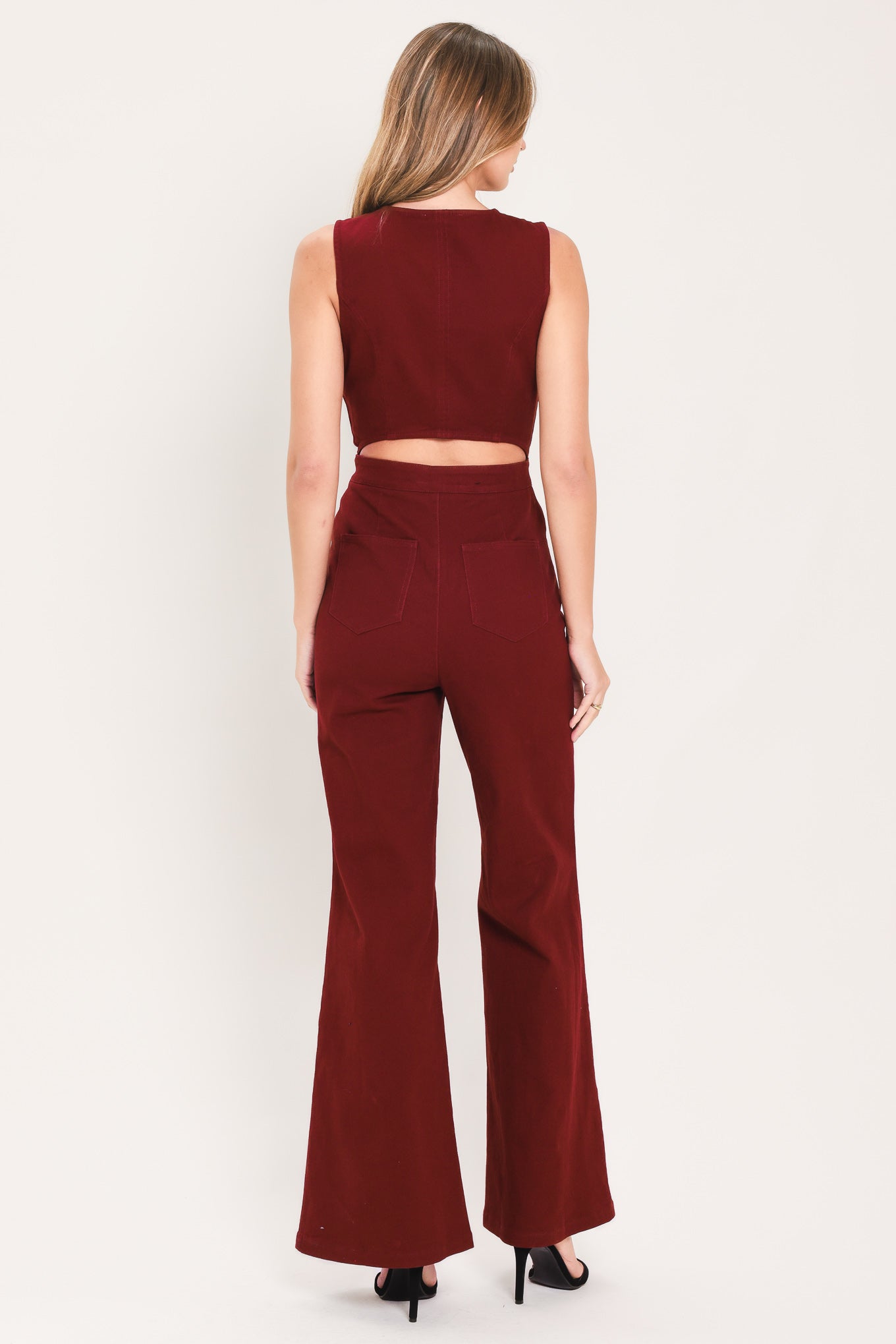 A woman wearing a sleeveless, deep burgundy jumpsuit with a V-neckline, front buttons, and wide-leg pants | Flying Tomato