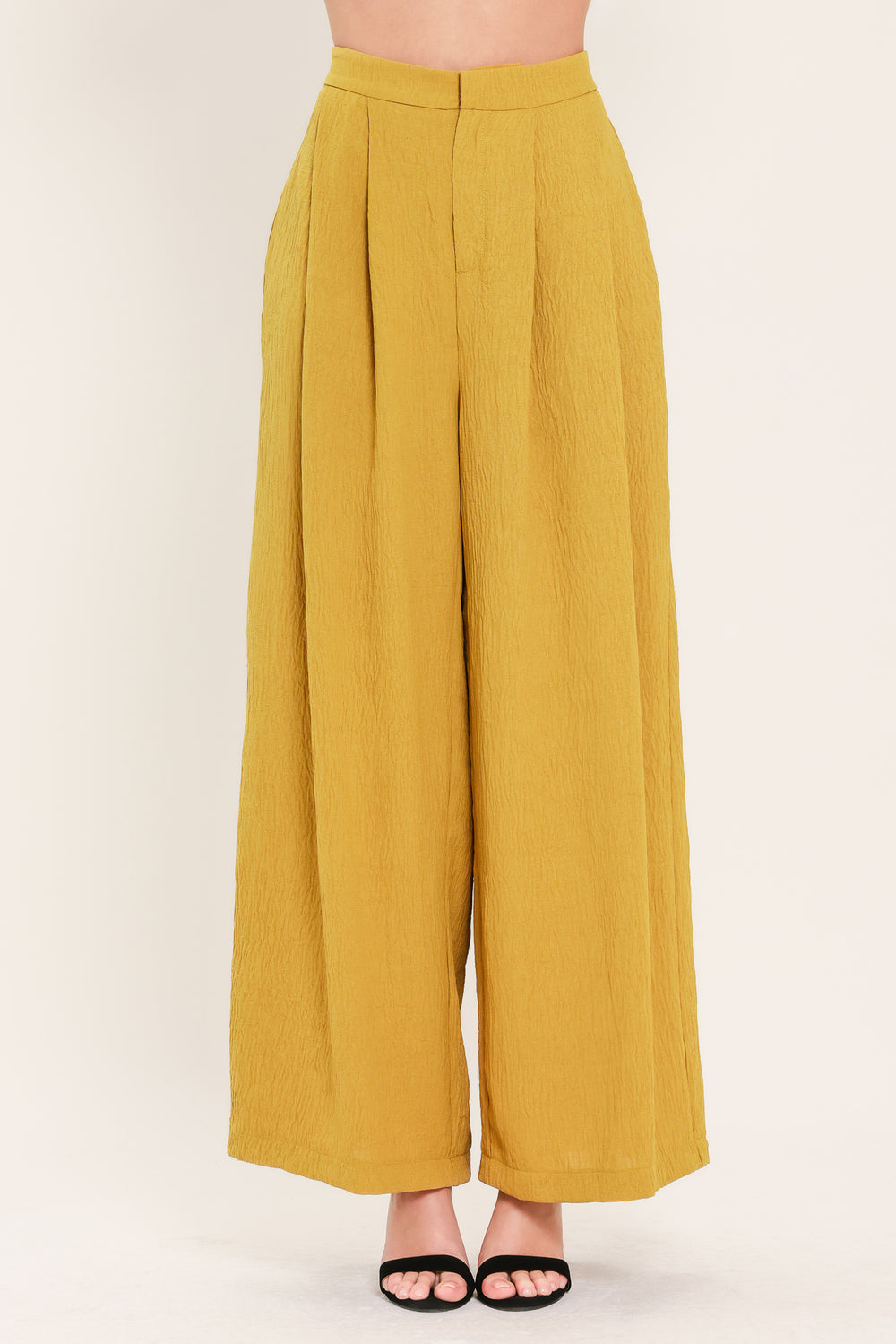 A person wearing high-waisted, wide-leg pleated trousers in a mustard yellow color | Flying Tomato