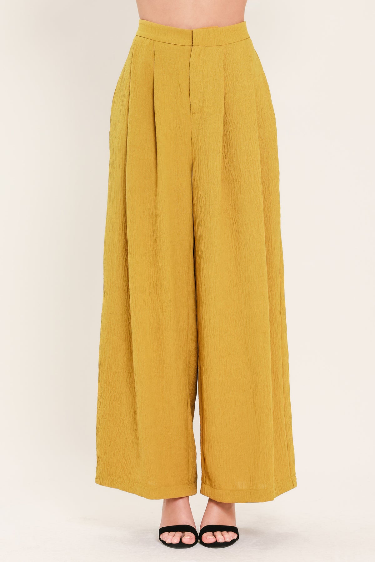 A person wearing high-waisted, wide-leg pleated trousers in a mustard yellow color | Flying Tomato
