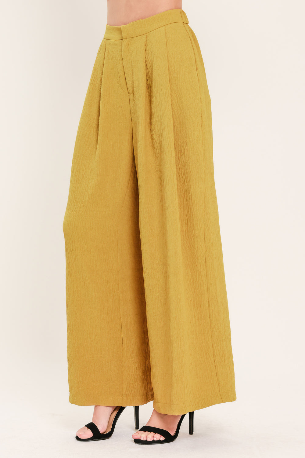 A person wearing high-waisted, wide-leg pleated trousers in a mustard yellow color | Flying Tomato