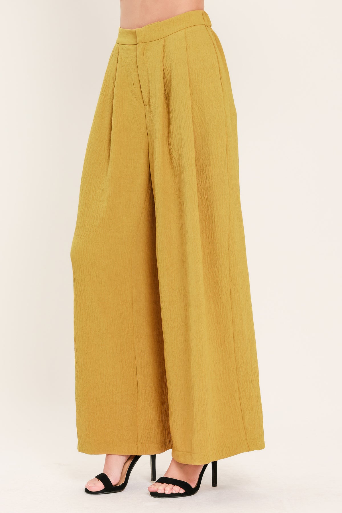 A person wearing high-waisted, wide-leg pleated trousers in a mustard yellow color | Flying Tomato