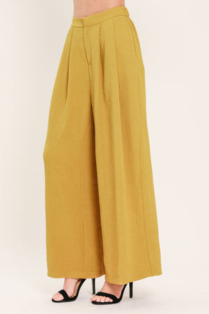 A person wearing high-waisted, wide-leg pleated trousers in a mustard yellow color | Flying Tomato