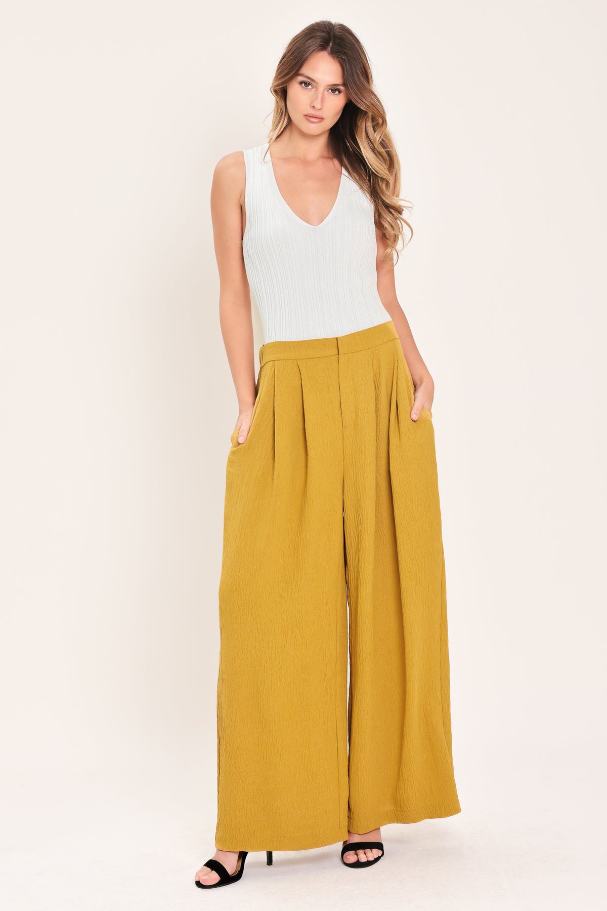 A person wearing high-waisted, wide-leg pleated trousers in a mustard yellow color | Flying Tomato