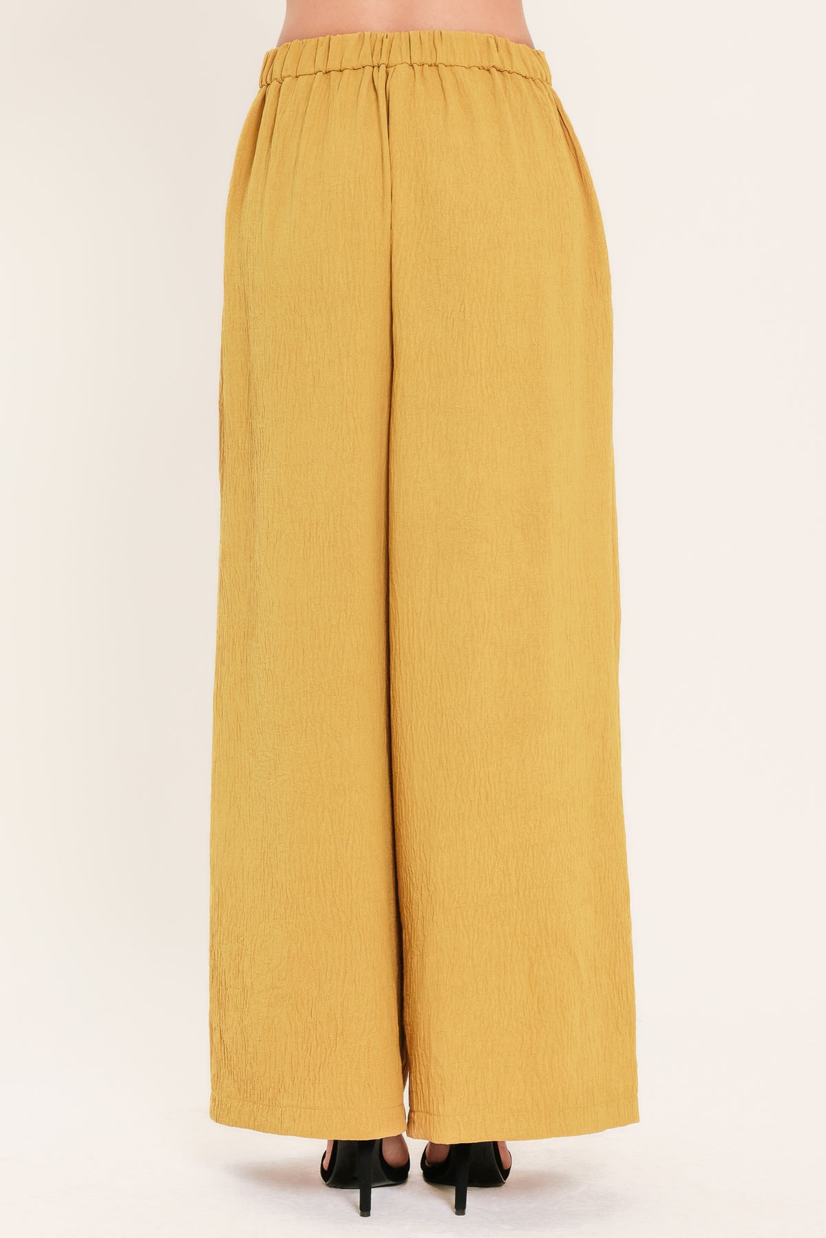 A person wearing high-waisted, wide-leg pleated trousers in a mustard yellow color | Flying Tomato