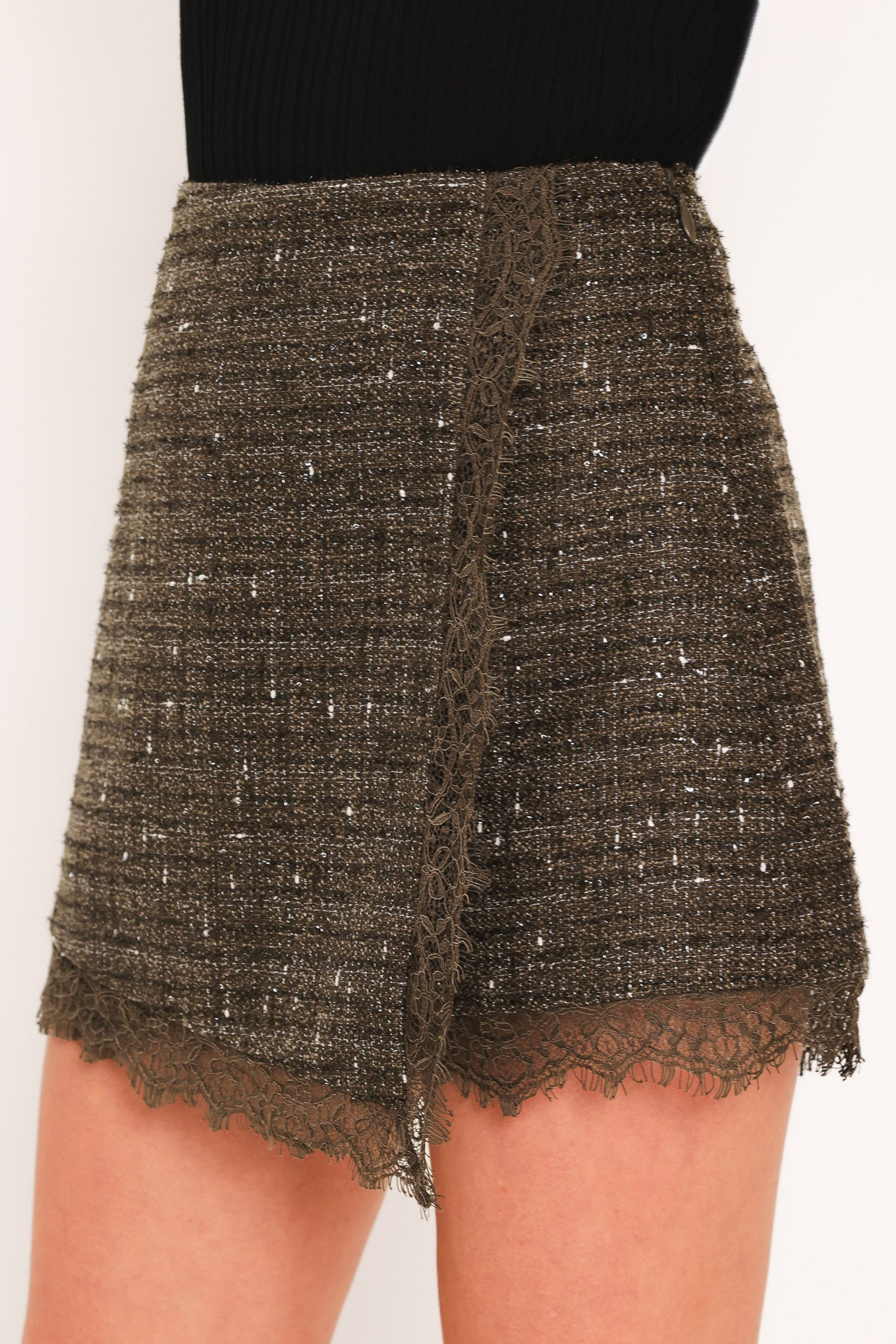 A close-up of a model wearing a dark brown tweed mini skort with a lace hem and a lace side detail | Flying Tomato