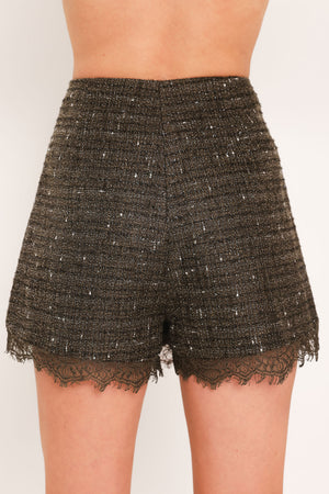 A close-up of a model wearing a dark brown tweed mini skort with a lace hem and a lace side detail | Flying Tomato