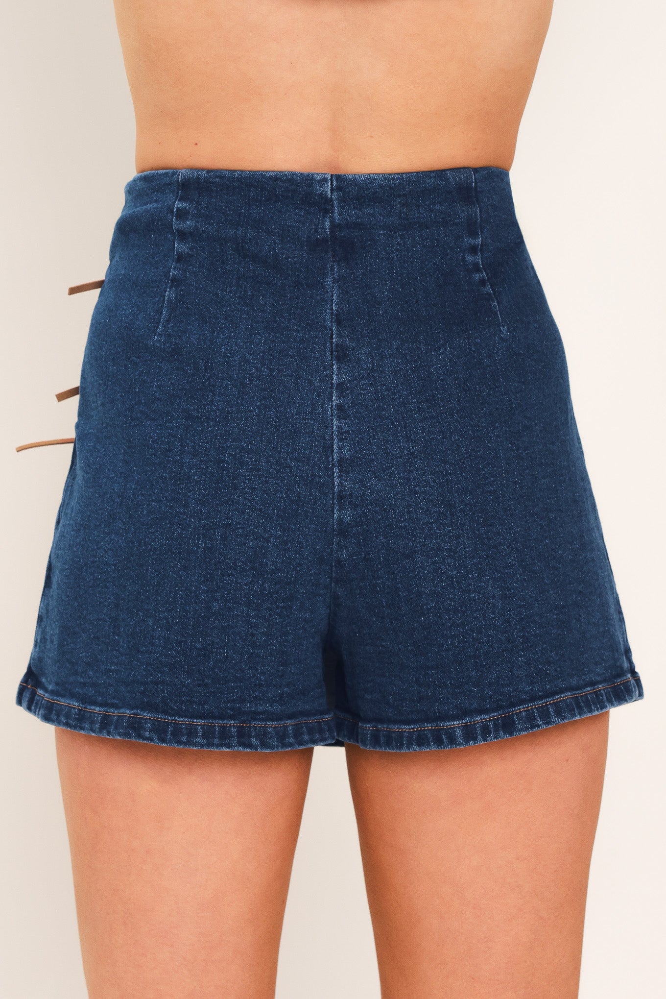 A woman wearing a blue denim mini skort featuring lace-up details on the side | Flying Tomato