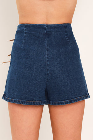 A woman wearing a blue denim mini skort featuring lace-up details on the side | Flying Tomato